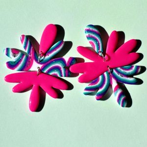 Paire de boucles d'oreilles en forme de "fleur maximaliste" abstraite asymétrique en trois parties. La puce forme un pétale rose uni vif. Le corps de la boucle est composé de cinq pétales au motif "à la dérive des astres", surmontant cinq autres pétales rose unie. L'autre boucle est en inversé (puce pétale d'accroche motif "à la dérive des astres", corps de cinq pétales rose uni et énorme pampille de cinq pétales au motif "à la dérive des astres").