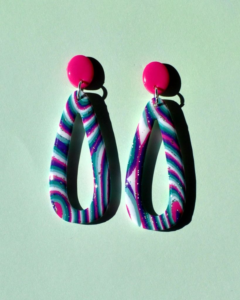 Paire de boucles d'oreilles en forme de "goutte" ajourée au motif "à la dérive des astres", surmontée d'une petite puce ovale rose vif.