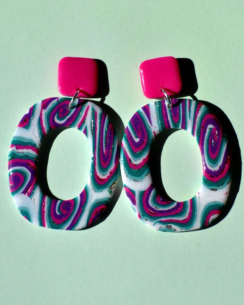 Paire de boucles d'oreilles en forme de "rectangle" rétro aux bords arrondis, ajourée au milieu, au motif "à la dérive des astres", surmontée d'une puce carrée rose vif.