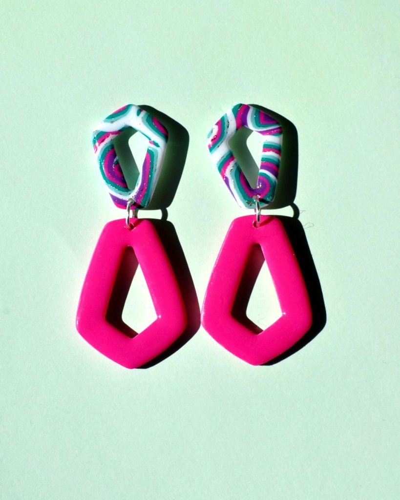 Paire de boucles d'oreilles composée de deux pentagones : un petit pentagone motif "à la dérive des astres", surmontant un plus grand pentagone inversé rose uni.