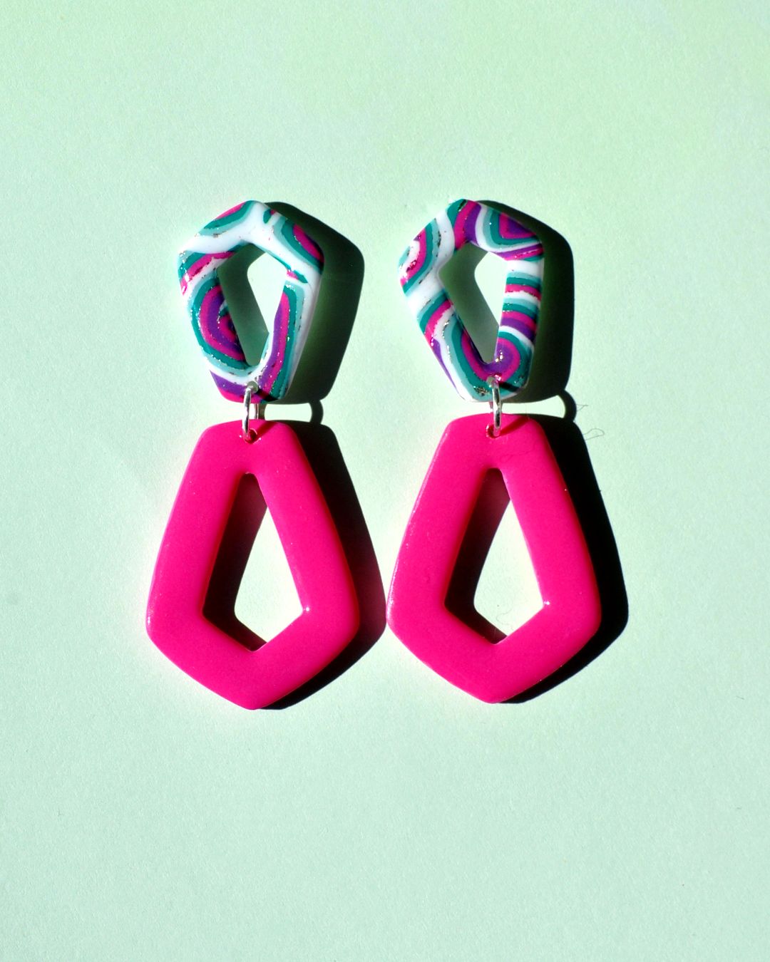 Paire de boucles d'oreilles composée de deux pentagones : un petit pentagone motif "à la dérive des astres", surmontant un plus grand pentagone inversé rose uni.