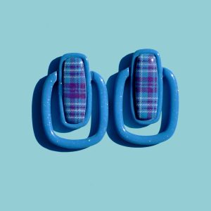Paire de boucles d'oreilles en forme de rectangle long, cerclé d'un autre rectangle plus bas, plus fin arrondi. Il y a un jour entre les deux rectangles. La paire de boucles d'oreilles est unie, d'un bleu glacé. Le premier rectangle possède un rectangle en relief "cabochon" au motif à carreaux "check" lie-de-vin et blancs.