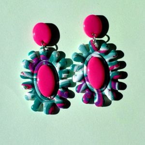 Paire de boucles d'oreilles en forme de fleur abstraite au motif "à la dérive des astres". Le cœur de la "fleur" est un ovale en longueur, en relief uni rose vif. La boucle est surmontée d'une puce ovale unie, rose vif.