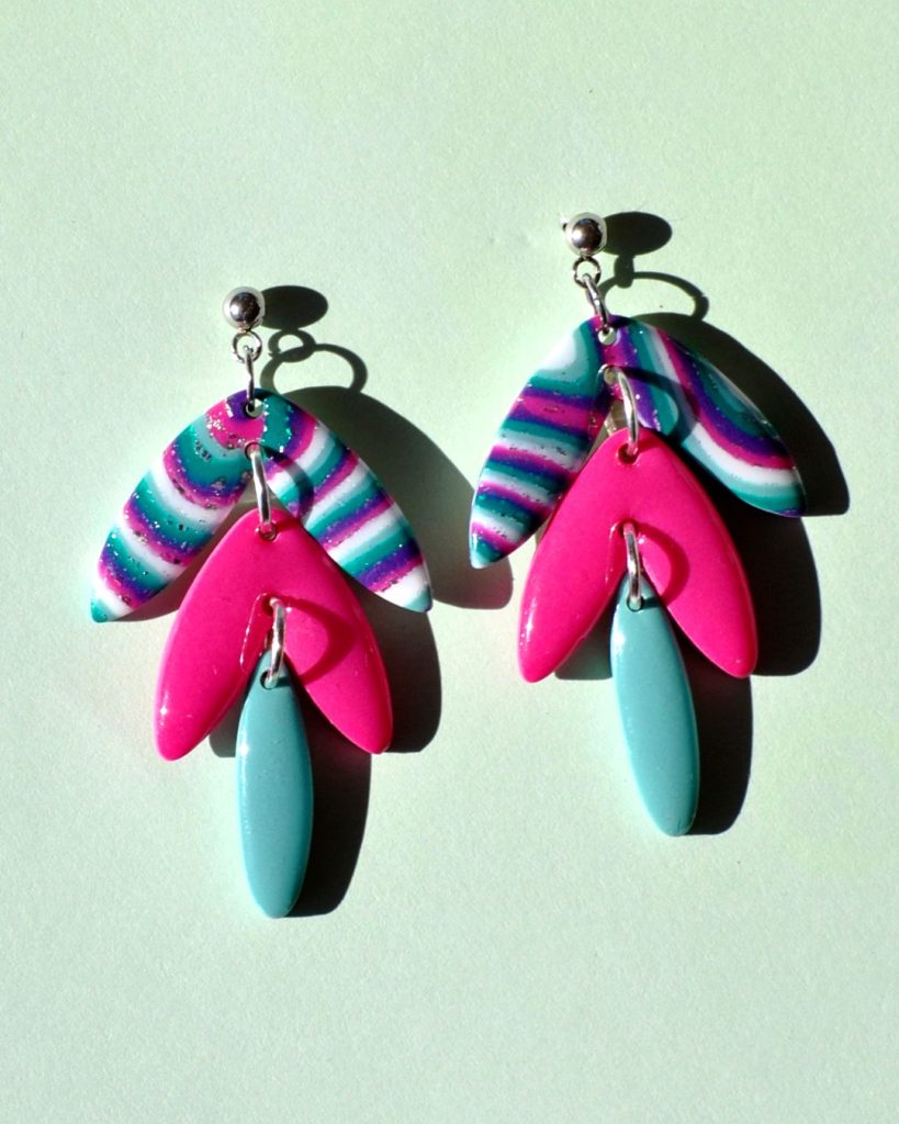 Paire de boucles d'oreilles en quatre parties: une petite puce ronde en acier inoxydable surmonte une forme de "glycine" en trois parties. Le double pétales le plus large, en haut, est au motif "à la dérive des astres". Le double pétales du milieu, de taille moyenne est uni, rose vif. Le dernier pétale unique est uni, vert vague marine.