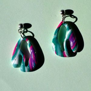 Petite paire de boucles d'oreilles en deux parties. Une petite puce en acier inoxydable surmonte une forme abstraite au motif "à la dérive des astres".