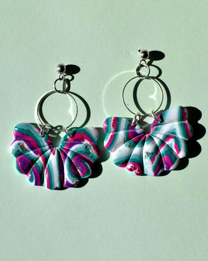 Paire de boucles d'oreilles en trois parties. Une petite puce en acier inoxydable, surmontant un cercle en acier inoxydable, surmontant une "moitié de fleur" ou un "papillon" au motif "à la dérive des astres".