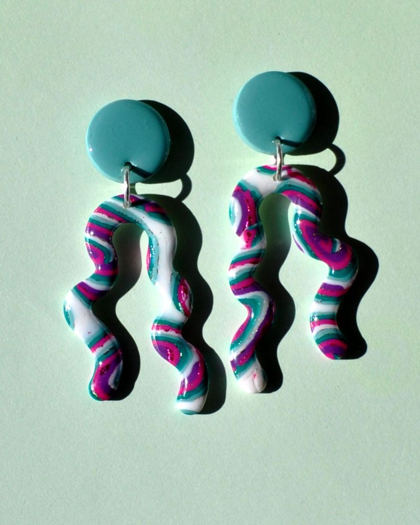 Paire de boucles d'oreilles en deux parties: une puce ronde unie vert vague marine surmonte un une ligne ondulante avec deux "bras" au motif "à la dérive des astres".