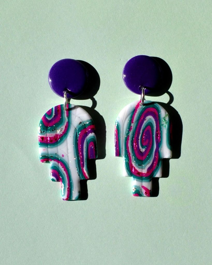 Paire de boucles d'oreilles en deux parties: une puce ronde unie violet profond surmonte un un arc à trois "branches" au motif "à la dérive des astres".