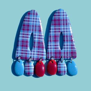 Paire de boucles d'oreilles triangulaire abstraite, ajourée au milieu, à carreaux "check" lie-de-vin et blancs. Sous le triangle tombent trois pampilles: une unie bleu glacé, une à carreaux et une unie lie-de-vin.