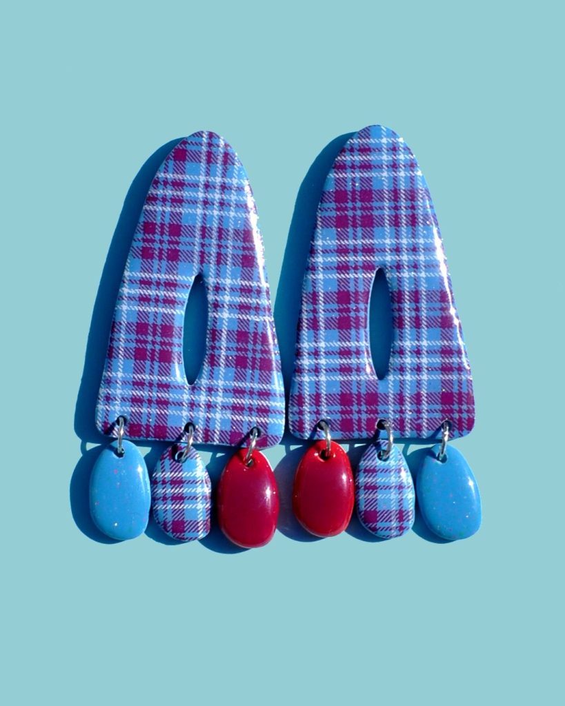 Paire de boucles d'oreilles triangulaire abstraite, ajourée au milieu, à carreaux "check" lie-de-vin et blancs. Sous le triangle tombent trois pampilles: une unie bleu glacé, une à carreaux et une unie lie-de-vin.
