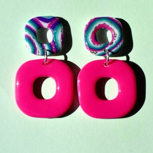 Paire de boucles d'oreilles duo de carrés aux bords arrondis. Un petit carré motif "à la dérive des astres" surmonte un plus gros carré rose vif uni.