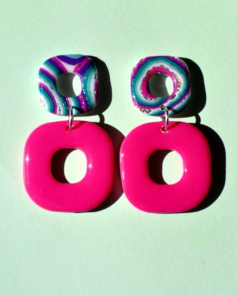 Paire de boucles d'oreilles duo de carrés aux bords arrondis. Un petit carré motif "à la dérive des astres" surmonte un plus gros carré rose vif uni.