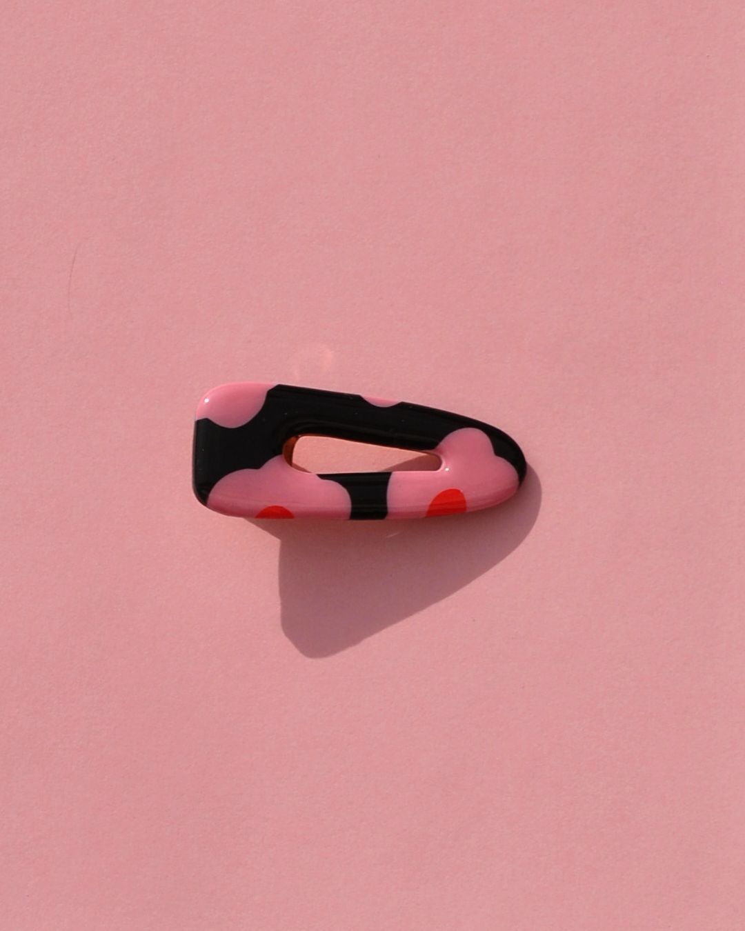 Barrette triangle classique aux bords arrondis, ajourée, au motif à fleurs roses à six pétales à cœur rouge sur fond noir.