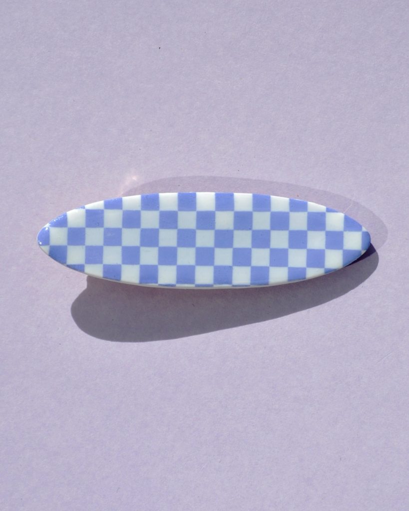 Barrette ellipse forme "planche de surf", au motif damier violet pâle sur fond blanc.