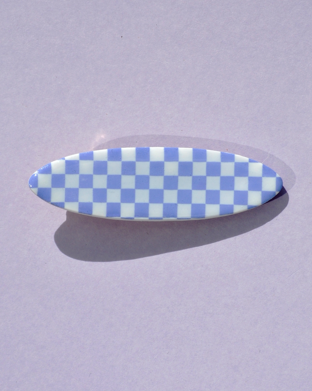 Barrette ellipse forme "planche de surf", au motif damier violet pâle sur fond blanc.