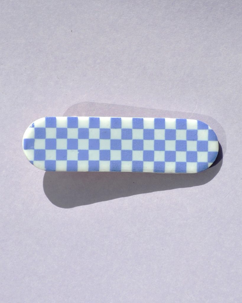 Barrette rectangle arrondi, au motif damier violet pâle sur fond blanc.