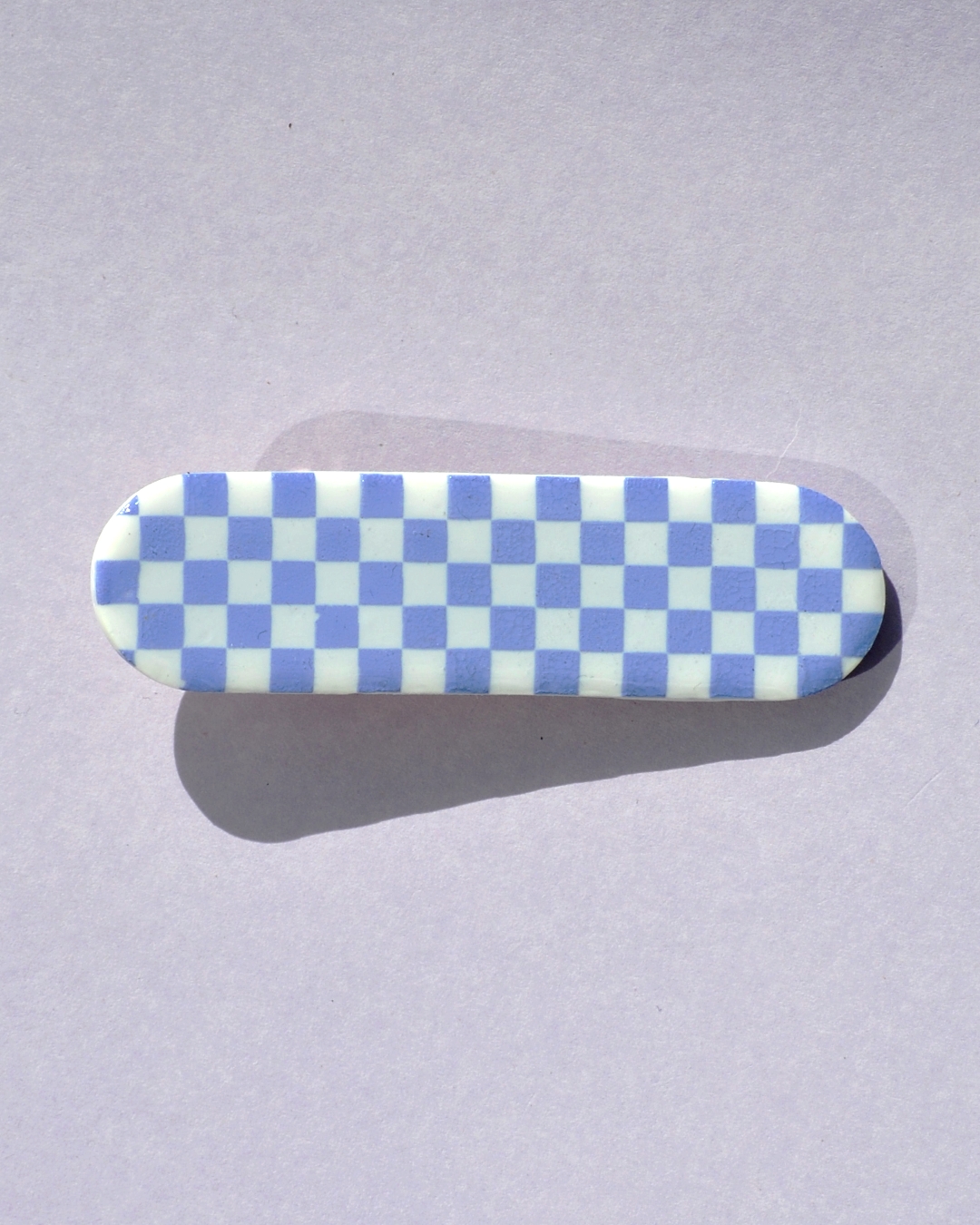 Barrette rectangle arrondi, au motif damier violet pâle sur fond blanc.