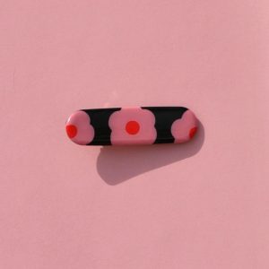 Barrette rectangle arrondi, au motif à fleurs roses à six pétales à cœur rouge sur fond noir.