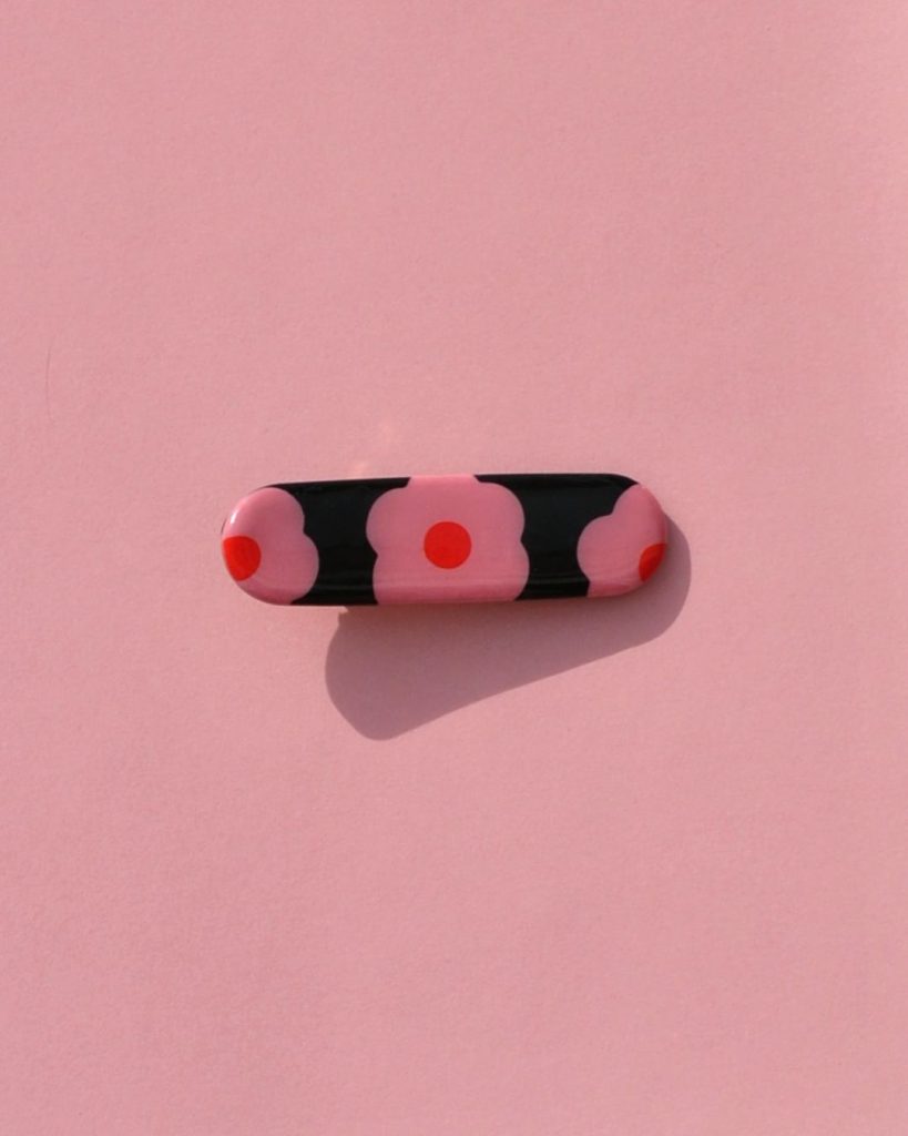 Barrette rectangle arrondi, au motif à fleurs roses à six pétales à cœur rouge sur fond noir.