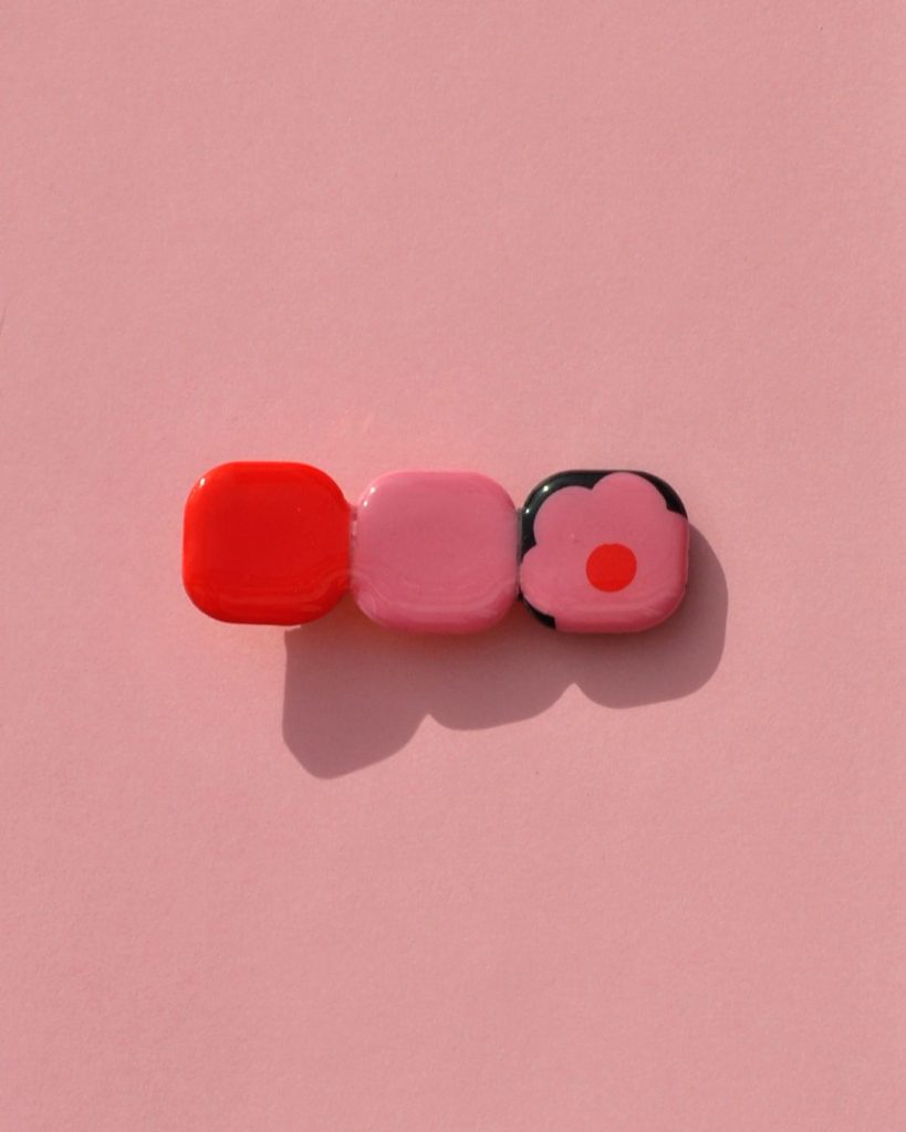 Barrette composée de trois carrés retro, un rouge vif, un rose et un fond noir avec une fleur rose à cœur rouge.