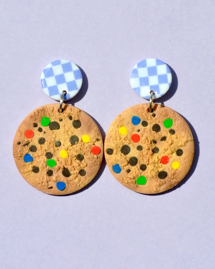Paire de boucles d'oreilles en forme de cookie géant aux smarties colorées. Une puce en pâte polymère blanche à carreaux violets clairs surmonte la boucle.