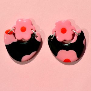 Paire de boucles d'oreilles en forme de courbe épaisse. Une puce fleur rose à cœur rouge vif surmonte une boucle à fond noir avec les mêmes fleurs roses à cœur rouge.