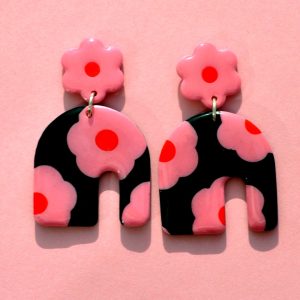 Paire de boucles d'oreilles énorme arc asymétrique. Une puce fleur rose à cœur rouge vif surmonte une boucle à fond noir avec les mêmes fleurs roses à cœur rouge.