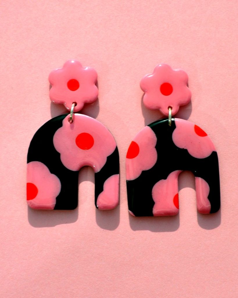 Paire de boucles d'oreilles énorme arc asymétrique. Une puce fleur rose à cœur rouge vif surmonte une boucle à fond noir avec les mêmes fleurs roses à cœur rouge.