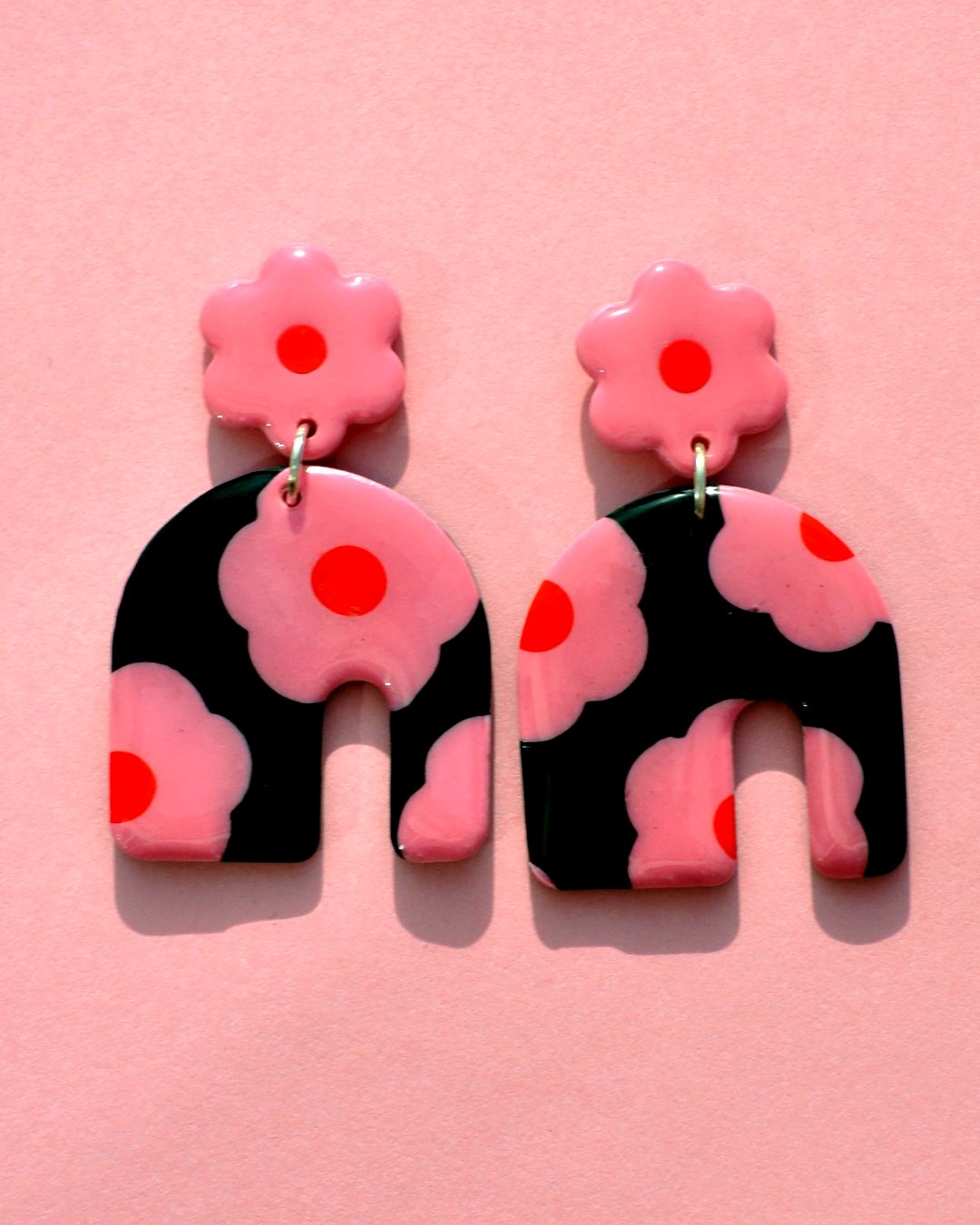 Paire de boucles d'oreilles énorme arc asymétrique. Une puce fleur rose à cœur rouge vif surmonte une boucle à fond noir avec les mêmes fleurs roses à cœur rouge.