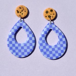 Paire de boucles d'oreilles d'énorme goutte dodue. La paire de boucles d'oreilles est ajourée au centre d'une goutte de taille moyenne. Une puce cookie surmonte une boucle motif damier violet soutenu sur fond violet pâle.
