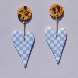 Paire de boucles d'oreilles en forme de cœur asymétrique allongé. Une puce cookie surmonte une tige en acier inoxydable argentée, surmontant la boucle au motif damier violet pâle sur fond blanc.