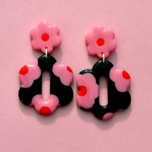 Paire de boucles d'oreilles en forme de grosse fleur à six pétales. La paire de boucles d'oreilles est ajourée au centre d'un ovale très allongé. Une puce fleur rose à cœur rouge vif surmonte une boucle à fond noir avec les mêmes fleurs roses à cœur rouge.