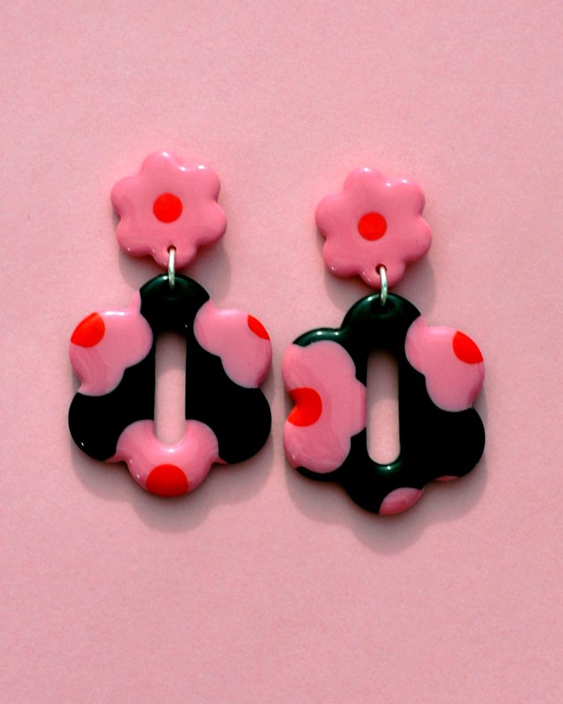 Paire de boucles d'oreilles en forme de grosse fleur à six pétales. La paire de boucles d'oreilles est ajourée au centre d'un ovale très allongé. Une puce fleur rose à cœur rouge vif surmonte une boucle à fond noir avec les mêmes fleurs roses à cœur rouge.