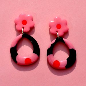 Paire de boucles d'oreilles en forme de goutte dodue en finesse. La paire de boucles d'oreilles est ajourée au centre d'une goutte large. Une puce fleur rose à cœur rouge vif surmonte une boucle à fond noir avec les mêmes fleurs roses à cœur rouge.