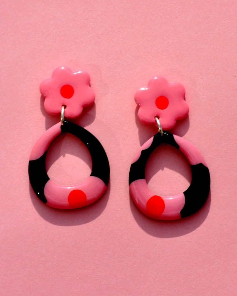 Paire de boucles d'oreilles en forme de goutte dodue en finesse. La paire de boucles d'oreilles est ajourée au centre d'une goutte large. Une puce fleur rose à cœur rouge vif surmonte une boucle à fond noir avec les mêmes fleurs roses à cœur rouge.