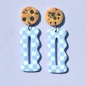 Paire de boucles d'oreilles en forme "petit lu" festonné allongé. La paire de boucles d'oreilles est ajourée au centre d'une ellipse très fine. Une puce cookie surmonte une boucle motif damier blanc sur fond violet pâle.