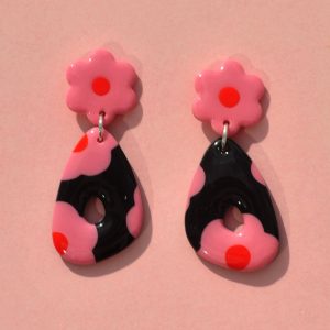 Paire de boucles d'oreilles duo de forme abstraite rétro. Une puce fleur rose à cœur rouge vif surmonte un "triangle" abstrait ajouré à fond noir avec les mêmes fleurs roses à cœur rouge.
