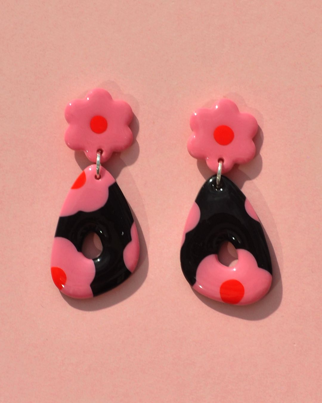 Paire de boucles d'oreilles duo de forme abstraite rétro. Une puce fleur rose à cœur rouge vif surmonte un "triangle" abstrait ajouré à fond noir avec les mêmes fleurs roses à cœur rouge.
