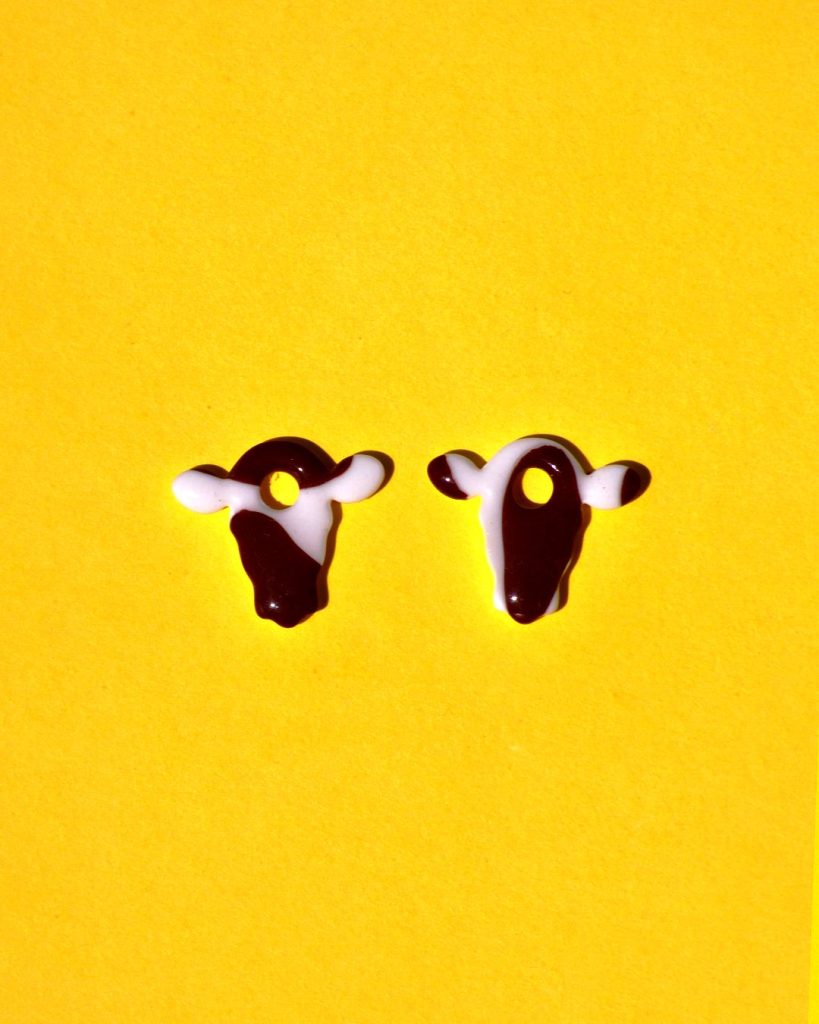 Pampilles interchangeables en forme de petite tête de vache, avec tâches de vache brunes sur fond blanc.