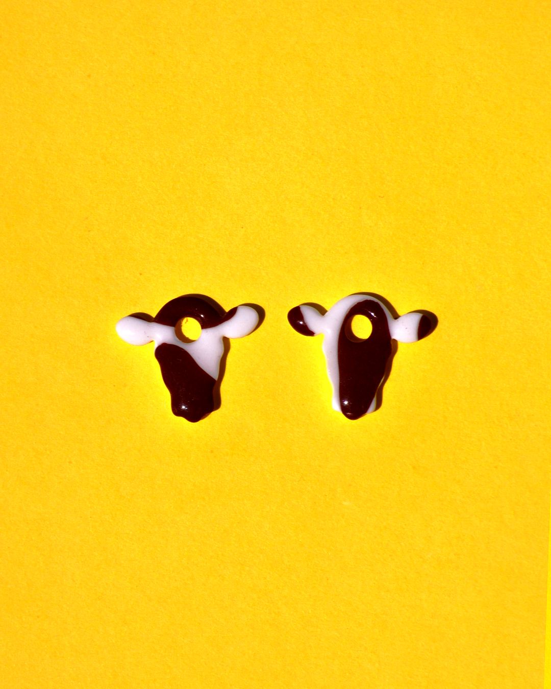 Pampilles interchangeables en forme de petite tête de vache, avec tâches de vache brunes sur fond blanc.