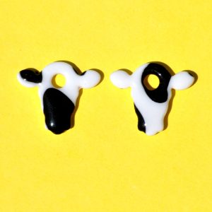 Pampilles interchangeables en forme de petite tête de vache, avec tâches de vache noires sur fond blanc.