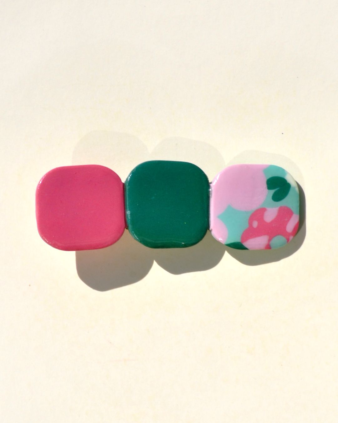 Barrette composée de trois carrés retro, un rouge-rose, un vert foncé et un motif floral.