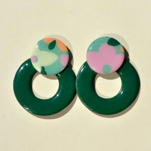 Paire de boucles d'oreilles en forme de cercle ajouré. Une grosse puce ronde en relief est collée sur le haut de la boucle. La boucle est unie verte foncée. La "puce" ronde est au motif floral printanier.