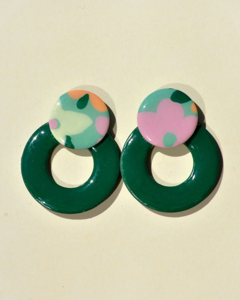 Paire de boucles d'oreilles en forme de cercle ajouré. Une grosse puce ronde en relief est collée sur le haut de la boucle. La boucle est unie verte foncée. La "puce" ronde est au motif floral printanier.