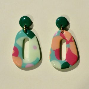 Paire de boucles d'oreilles en forme galet donut. La paire de boucles d'oreilles est ajourée au centre d'un long rectangle arrondi élancé. Une petite puce ronde verte foncée unie surmonte une boucle au motif floral printanier.