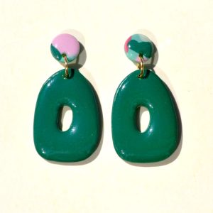 Petite paire de boucles d'oreilles en forme petit galet donut. La paire de boucles d'oreilles est ajourée au centre d'un petit rond abstrait. Une petite puce ronde motif floral printanier surmonte une boucle unie vert foncée.