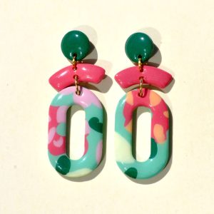 Paire de boucles d'oreilles en trois parties: la partie principale de la boucle est un ovale ajouré au motif floral printanier. Il est surmonté de deux petites parties formant comme un "chapeau de marin à pompon". La petite "visière" est rose-rouge unie. Le pompon est vert foncé.