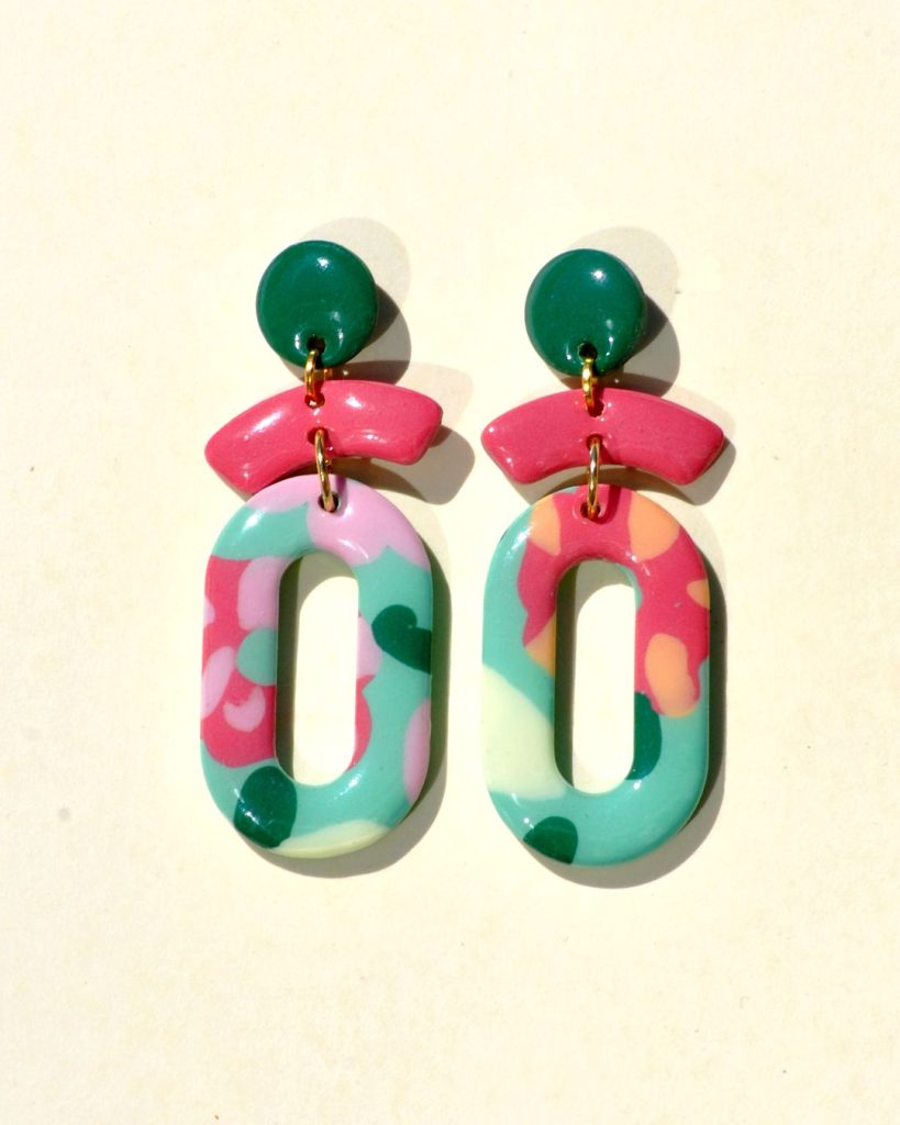 Paire de boucles d'oreilles en trois parties: la partie principale de la boucle est un ovale ajouré au motif floral printanier. Il est surmonté de deux petites parties formant comme un "chapeau de marin à pompon". La petite "visière" est rose-rouge unie. Le pompon est vert foncé.