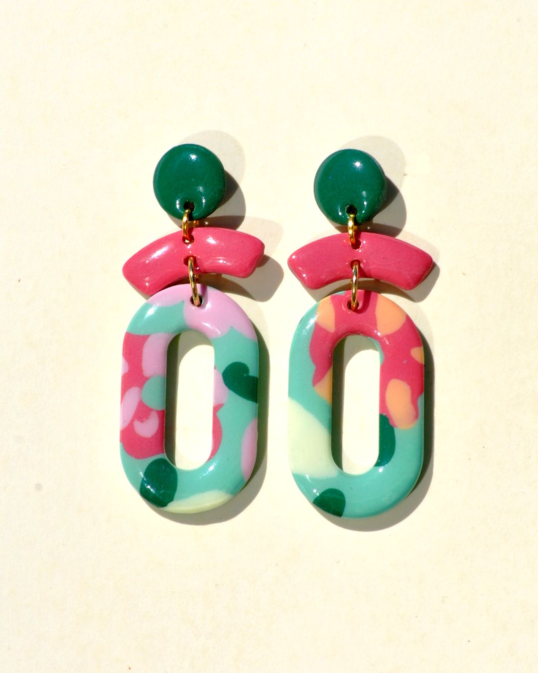 Paire de boucles d'oreilles en trois parties: la partie principale de la boucle est un ovale ajouré au motif floral printanier. Il est surmonté de deux petites parties formant comme un "chapeau de marin à pompon". La petite "visière" est rose-rouge unie. Le pompon est vert foncé.