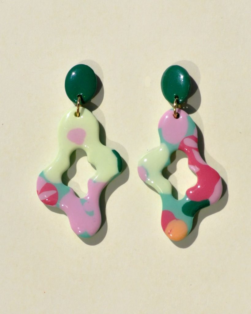 Paire de boucle d'oreilles abstraite au motif floral printanier, surmontée d'une puce ovale unie verte foncée.